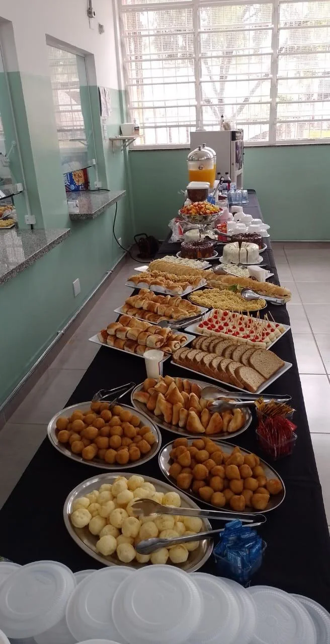 Mesa longa montada com salgados, pães, bolos e frutas em um evento